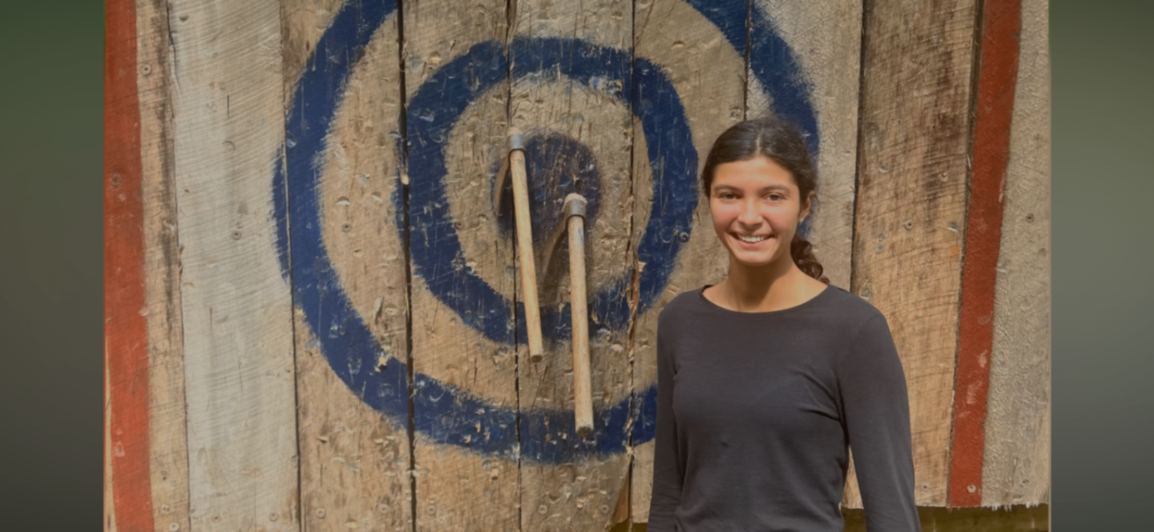 A student smiling by the axe throwing target at camp