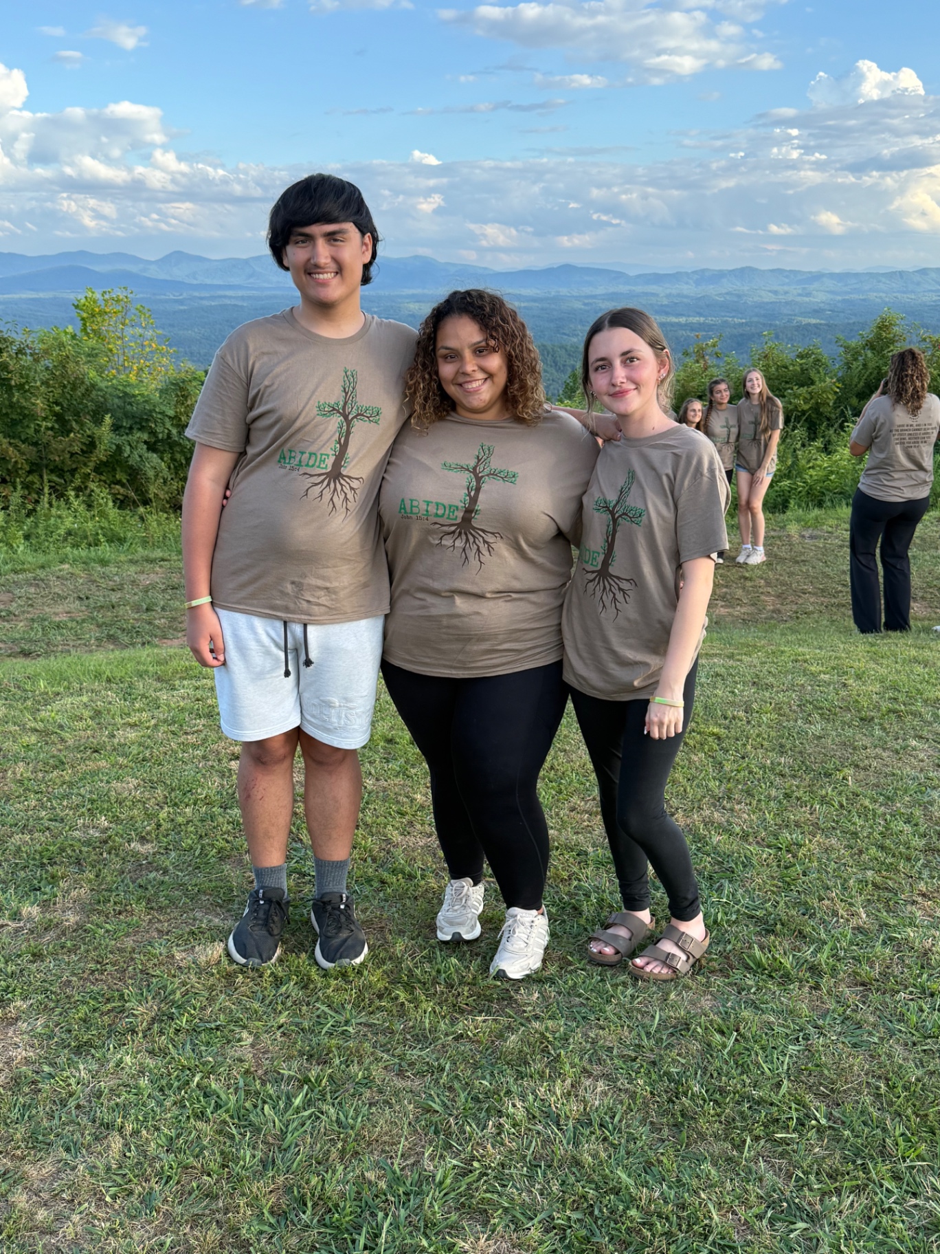 Three students in Abide shirts at a mountain overlook